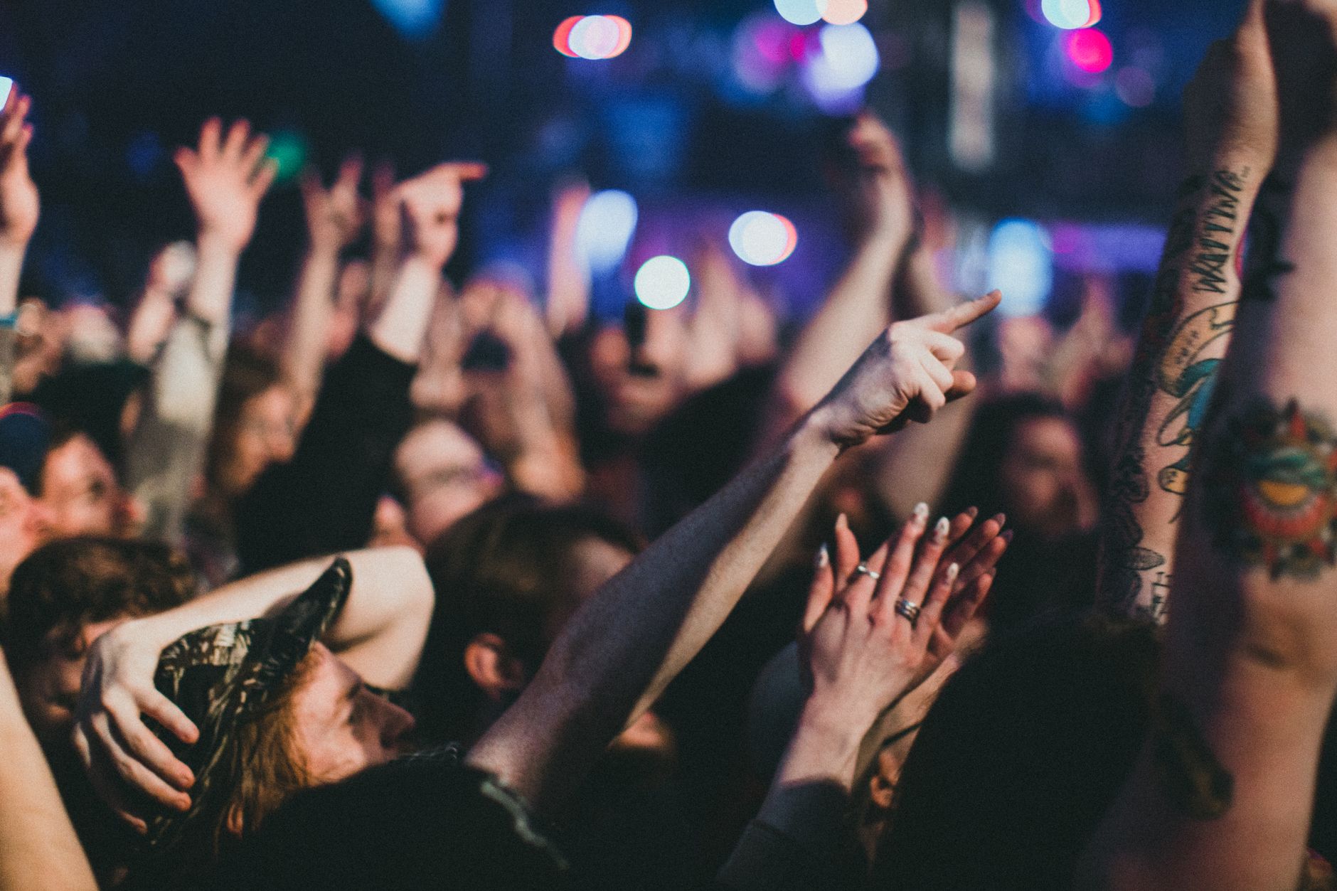 A concert crowd with raised hands under stage lights
